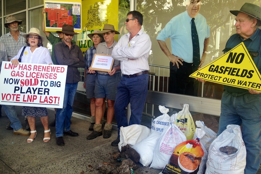 Farmers stand at front of MP's office holding ant CSG signs with manure at their feet.