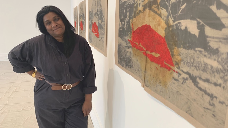 Sydney-based artist Shivanjani Lal leans towards a series of hanging photographs in a exhibition space