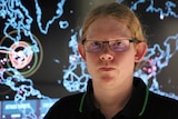 Close up of cyber expert Dr Peter Hannay against an electronic screen with a stylised world map on it.