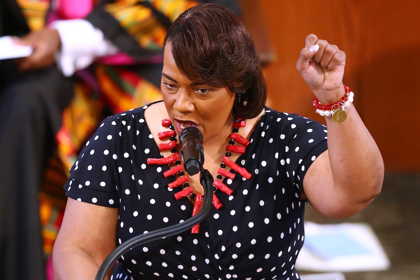 An African American woman wearing a spotted dress and red necklace