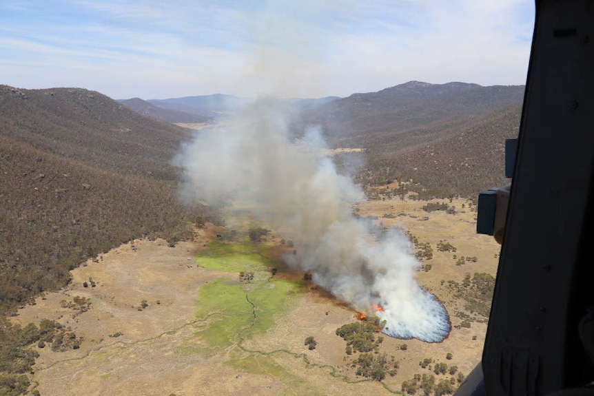 An aerial photograph from within a helicopter shows a patch of fire spreading through bushland