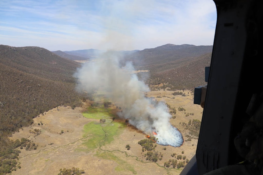 An aerial photograph from within a helicopter shows a patch of fire spreading through bushland