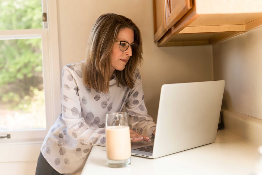 Lady standing at her kitchen bench using her lap top computer