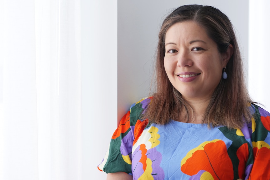 a woman in a brightly coloured top smiles into the camera