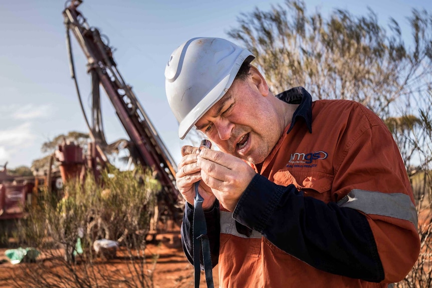 A geologist wearing high-vis workwear inspects drilling samples in the bush.