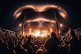 Festival-goers watch an act at a music gig. There are people on others shoulders and a whole lot of lights on the stage.