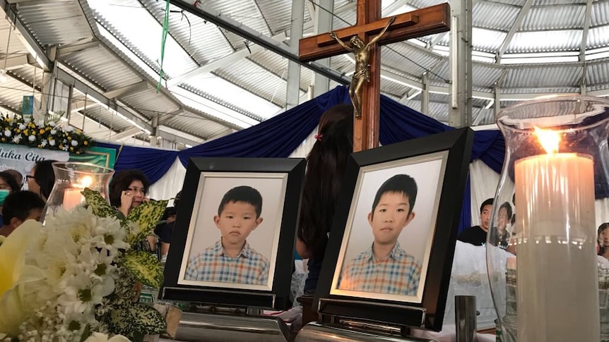 Framed photos of two young boys at a funeral with a cross in the background.