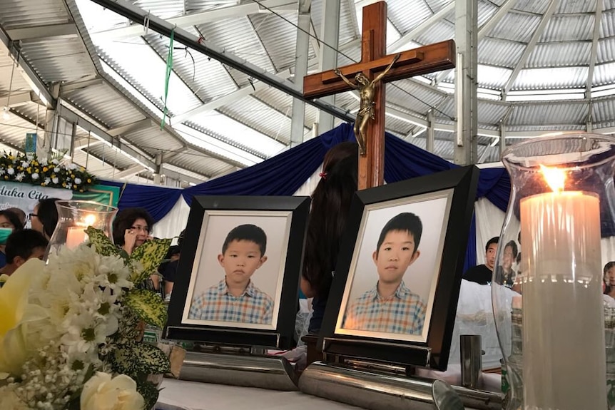 Framed photos of two young boys at a funeral with a cross in the background.