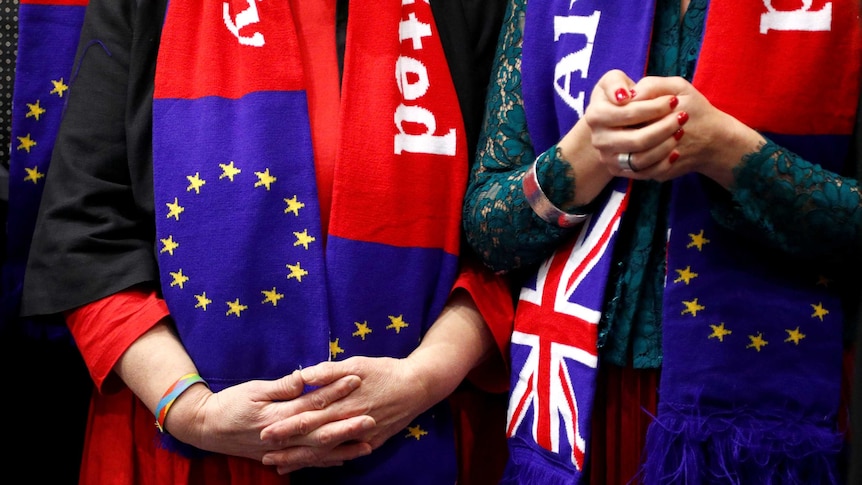 Close up of two women, hands clasped, wearing EU and UK flag scarves