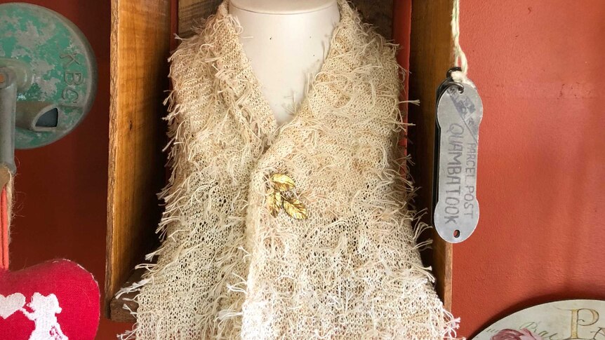 a scarf made out of tea bag strings on display at a cafe. description of scarf pinned on top