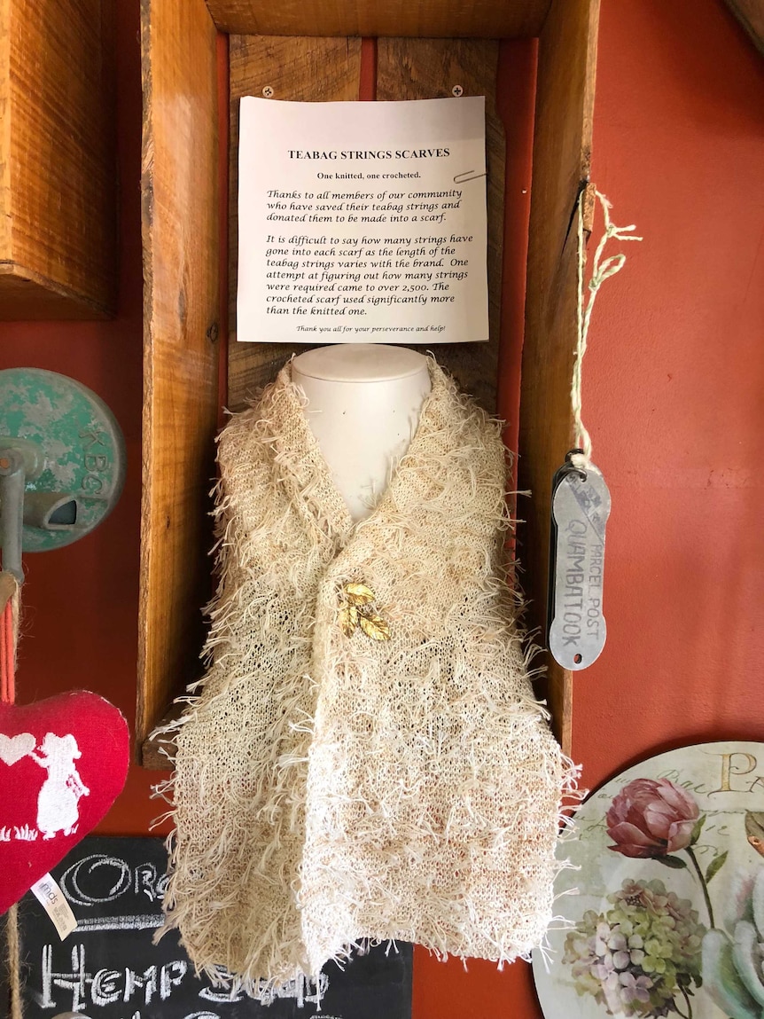 a scarf made out of tea bag strings on display at a cafe. description of scarf pinned on top