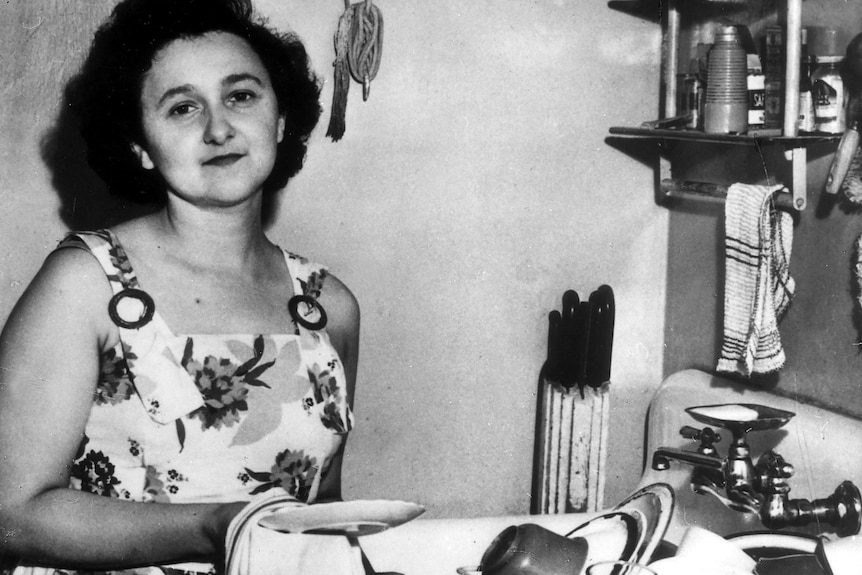 Ethel Rosenberg in a sundress in her kitchen doing the dishes.