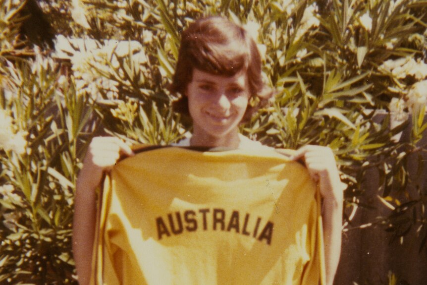 A grainy photograph of a young woman holding up a yellow soccer shirt with AUSTRALIA on the back 