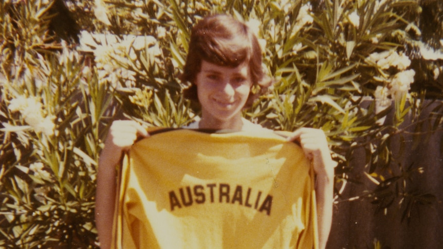 A grainy photograph of a young woman holding up a yellow soccer shirt with AUSTRALIA on the back 