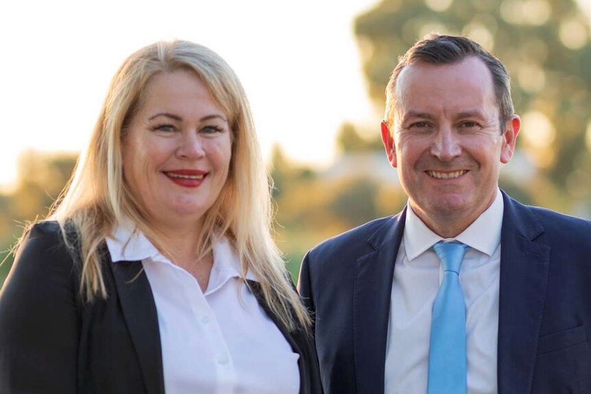 Colleen Yates and Mark McGowan stand together, smiling with trees and a lake in the background.