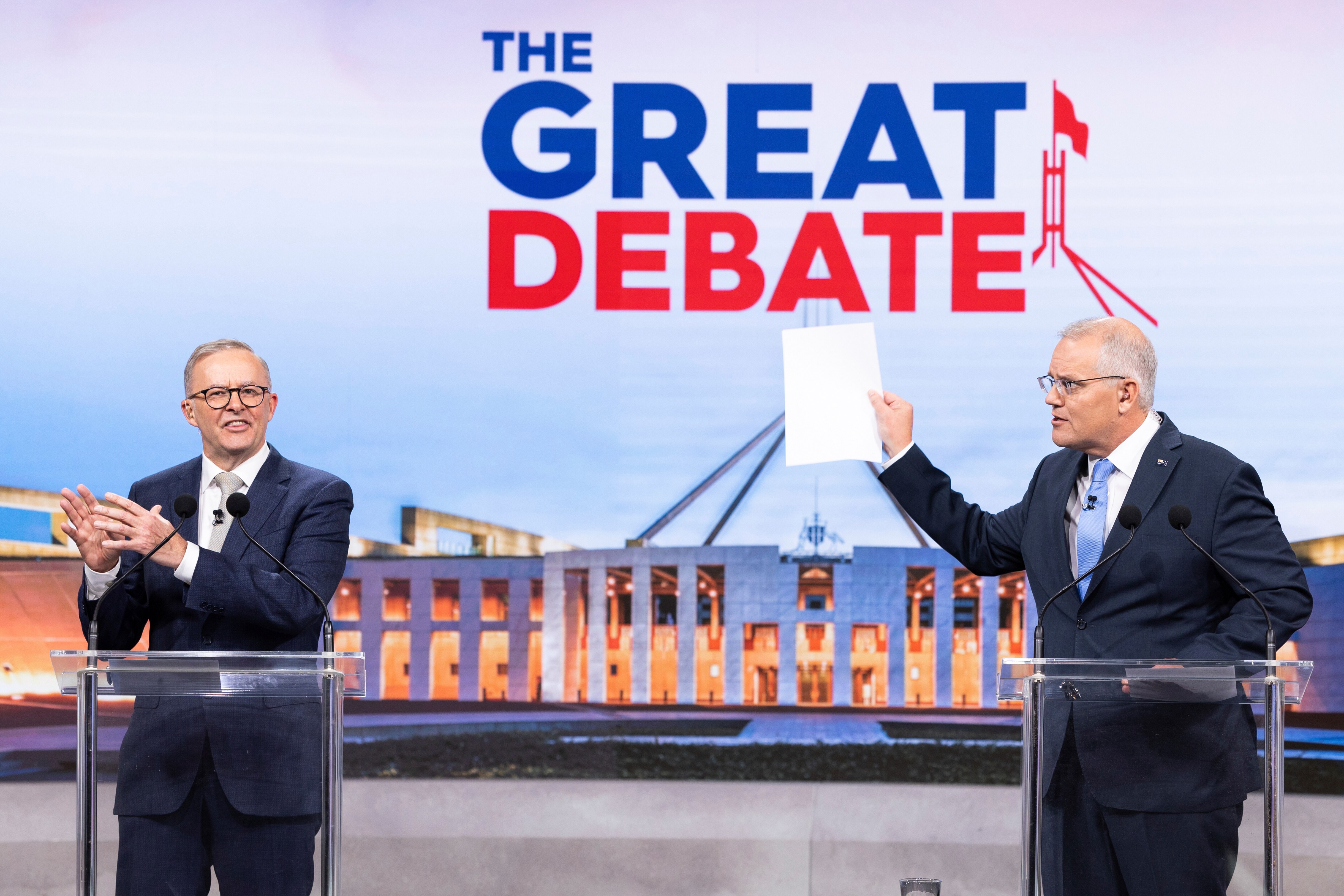 Scott Morrison holds up a piece of white paper as he stands next to Anthony Albanese with 'The Great Debate' sign behind them