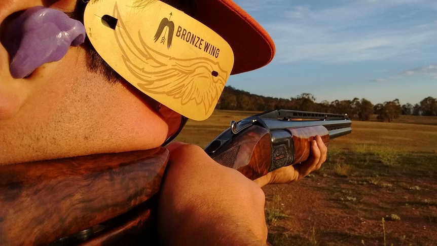 An unidentifiable man shoots a gun for clay-target shooting.