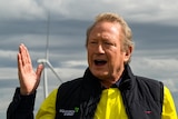 A close up of a middle-aged man in a high-viz polo shirt and padded vest, speaking outside and gesturing with one hand