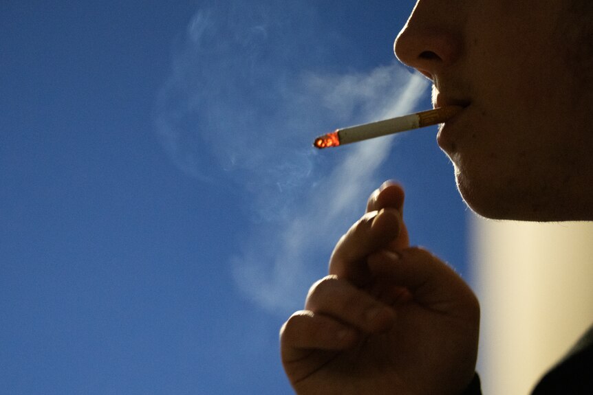 Silhouette of a man smoking a cigarette against a dark blue sky.