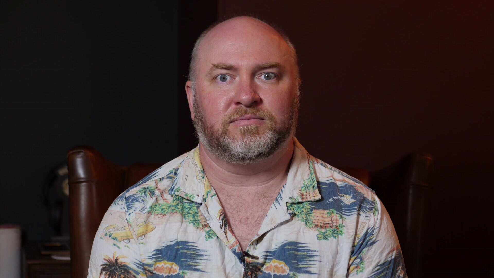 A bearded man in short sleeved Hawaiian shirt poses for a photo