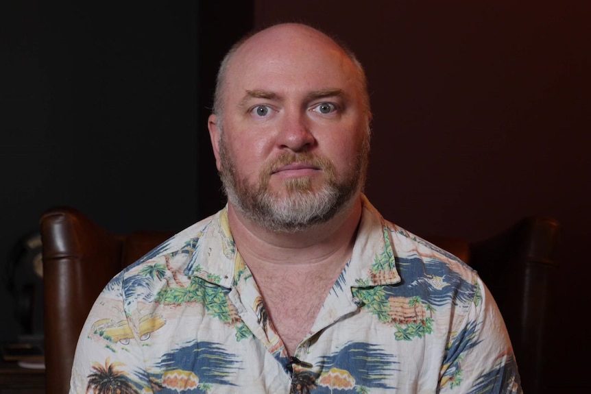 A bearded man in short sleeved Hawaiian shirt poses for a photo