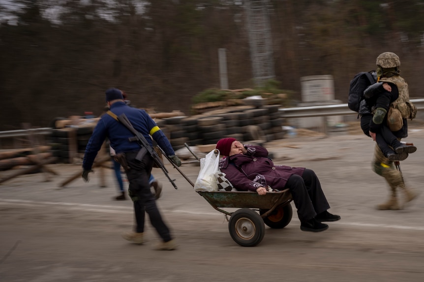 A Ukrainian soldier and a militia man help a fleeing family crossing the Irpin River.