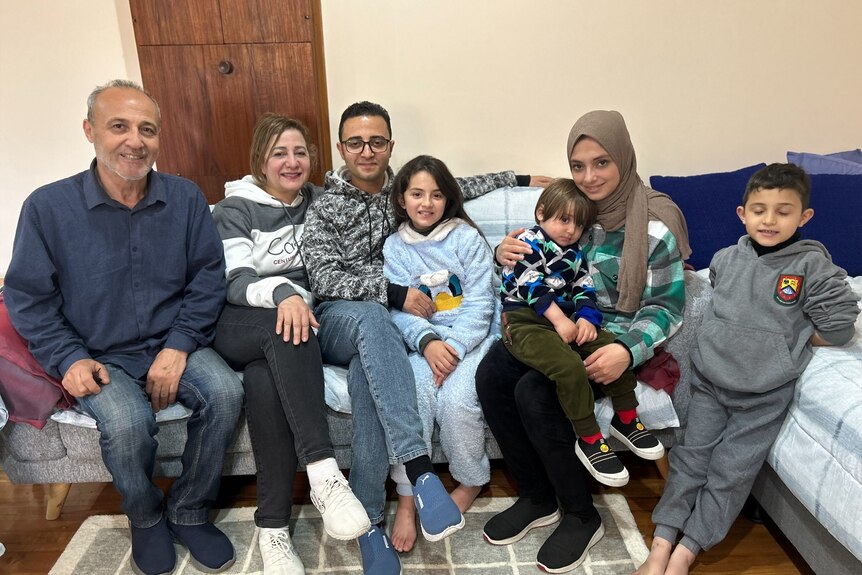 Rami's parents, his three children and wife sit on the couch of their home.