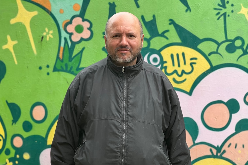 Imad Abulughud standing in front of a bright-coloured mural.