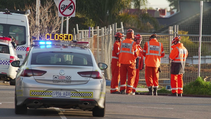 Five SES Rescue men wearing orange suits standing together at the scene of a crime