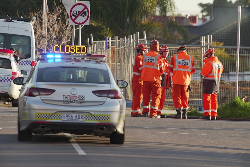 Five SES Rescue men wearing orange suits standing together at the scene of a crime