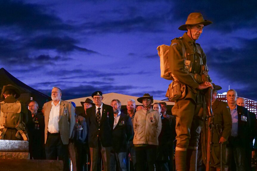 A soldier bows his head as people stand in silence at a dawn service