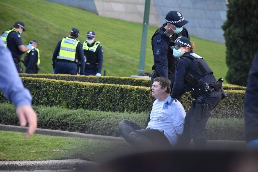 A man sits on the ground as he is arrested by Victoria Police at a protest at the Shrine of Remembrance.