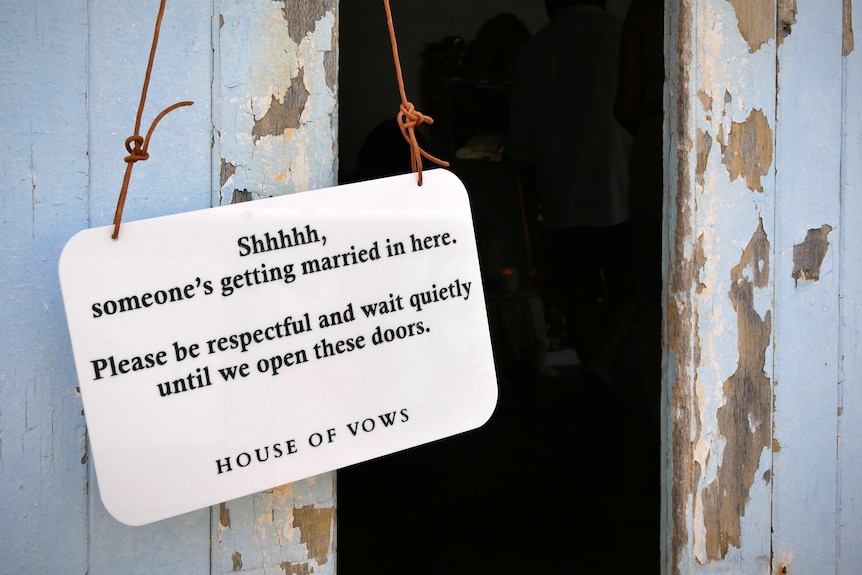 A sign hangs on a door, reading 'Shh, someone's getting married in here. Please be respectful and wait quietly..."