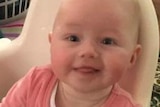A tight head shot of baby Isabella Martin smiling while sitting in a high chair.