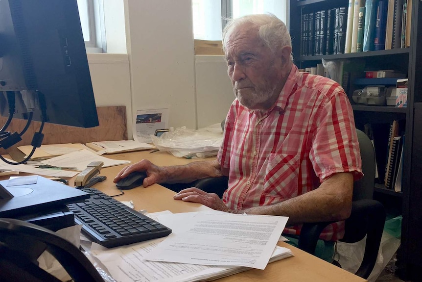 David Goodall sits at an office desk behind a computer.