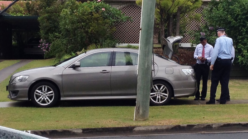 Grey police car, boot open with police at back and man hunched in back seat