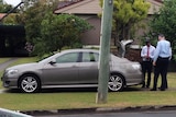Grey police car, boot open with police at back and man hunched in back seat