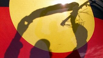 An Aboriginal elder silhouetted behind the Aboriginal flag. (Torsten Blackwood/AFP)