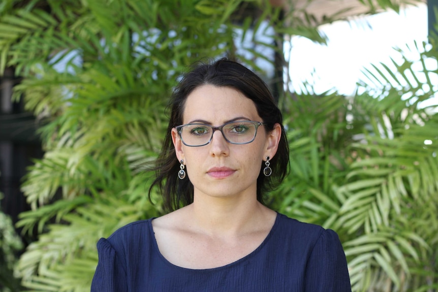 a middled aged woman with glasses in front of some shrubbery looking concerned.