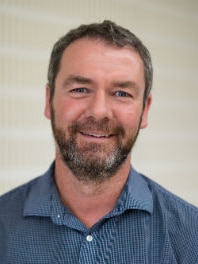 A man with short brown hair and a short beard, smiling