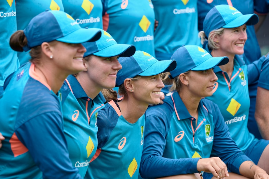 Meg Lanning is surrounded by teammates who are smiling for a photograph while in their training gear.