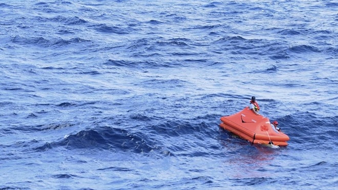 A boat is seen in the distance as a small life raft drifts in the ocean.