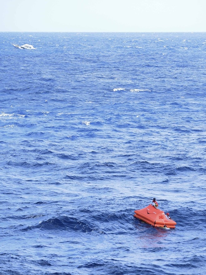 A boat is seen in the distance as a small life raft drifts in the ocean.