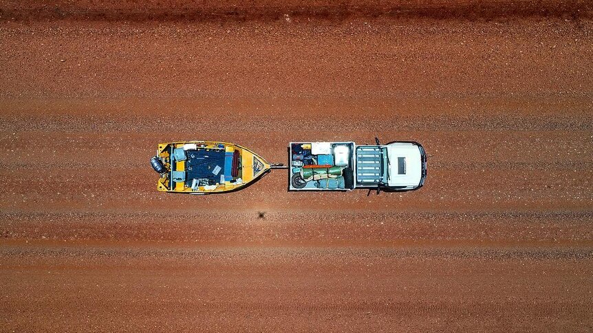 Aerial view of a car towing a boat in desert.