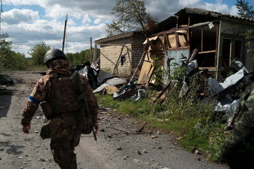 A Ukrainian serviceman from Dnipro-1 regiment walks past a damaged house 