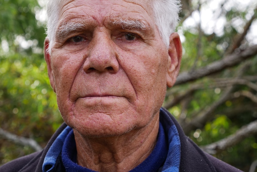 Close-up portrait of man in his 80s looking at the camera with a serious expression.