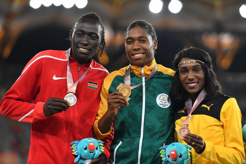 Three medallists stand together smiling.