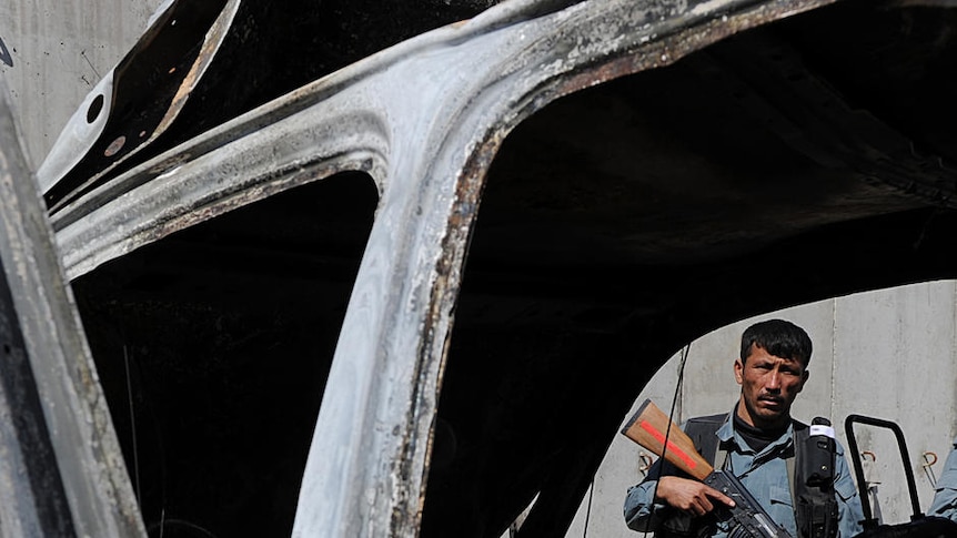 An Afghan policeman stands guard near the charred remains of a vehicle