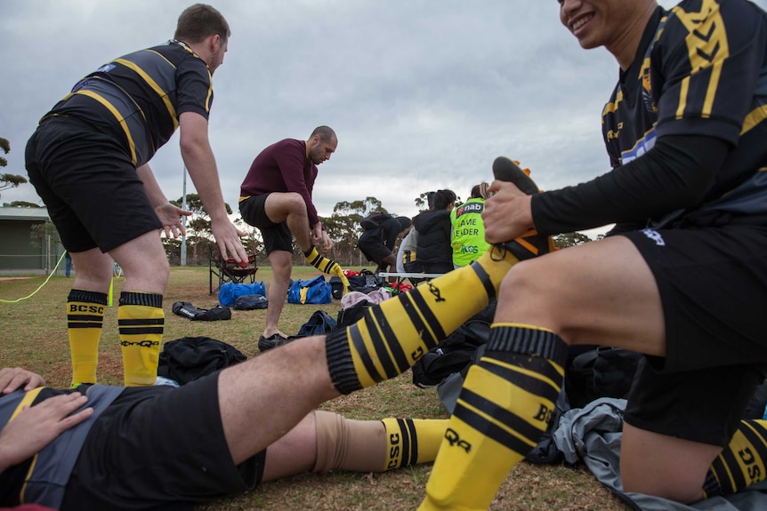 Josh pulls off his football socks, framed by other players helping each other removing boots.