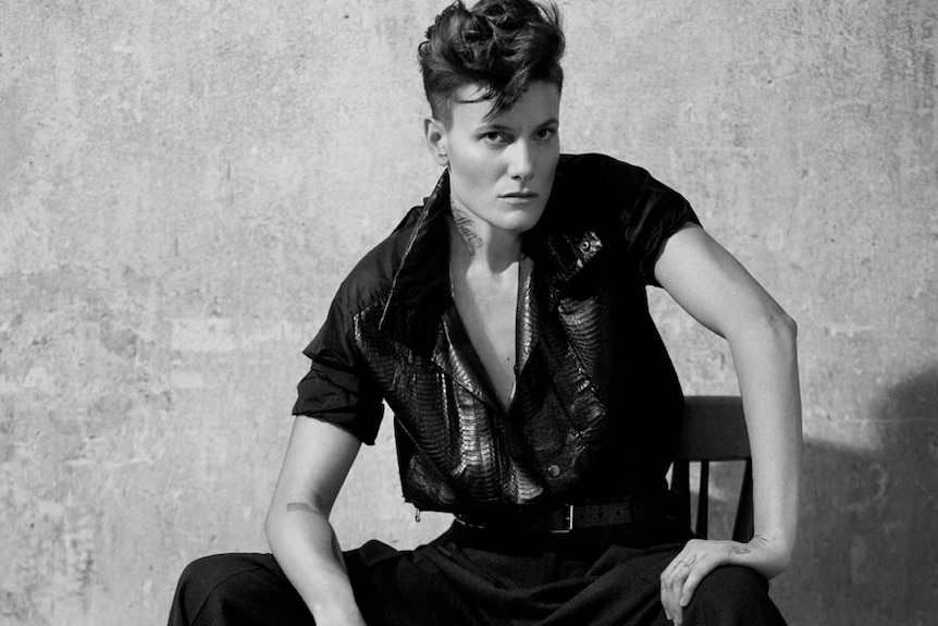 A black and white photo of female model Casey Legler posing while sitting on a stool.